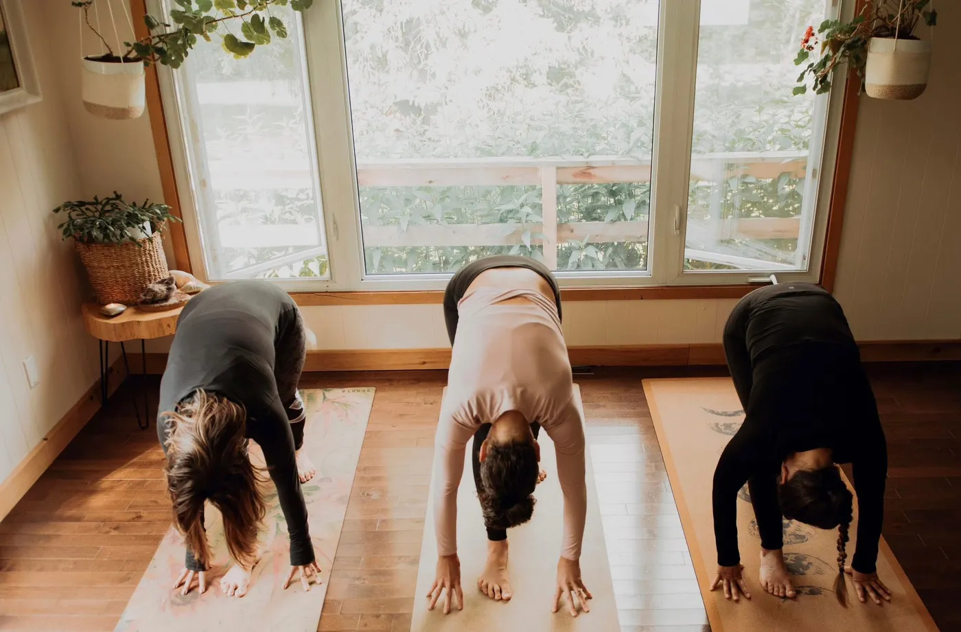 Three students in pyramid pose by the studio windows
